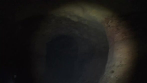 Woman Explores Stalactites Inside a Deep Dark Cave Illuminating with Flashlight alt