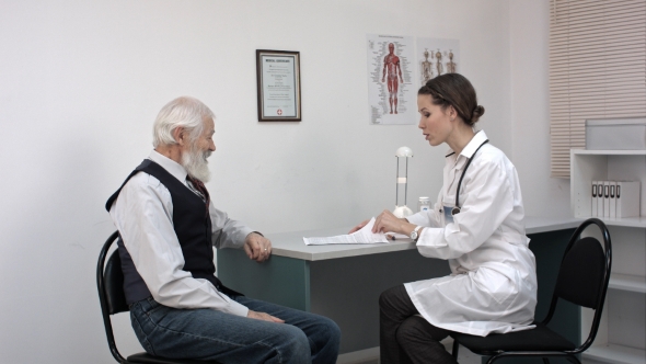 Doctor Talking To Her Male Senior Patient And Writing Something. alt