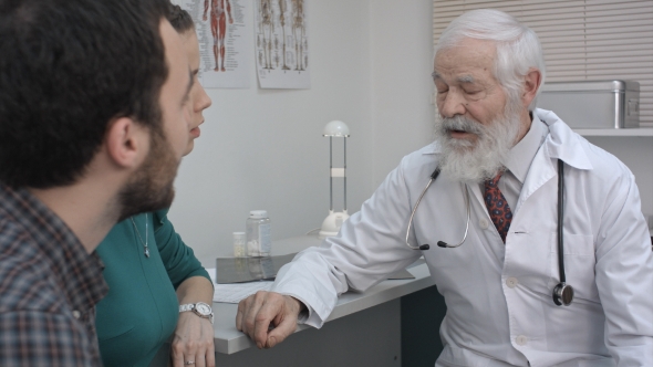 Doctor Meeting Couple And Offering Pills Medicine In Hospital Office. alt