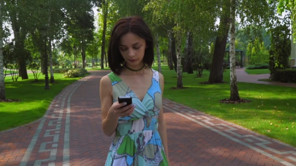 A Young Girl Goes On a Path In The Park And Gaining a Message On The Phone. alt