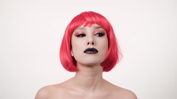 Portrait of Caucasian joyful stylish woman in pink wig smiling to camera on light background alt