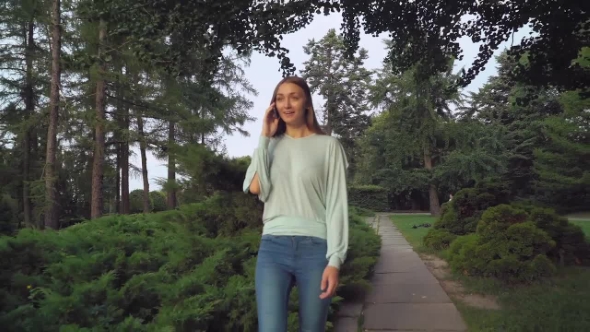 A Young Girl Is Skinny Park And Talking On The Phone, Smiles, Surprised. alt