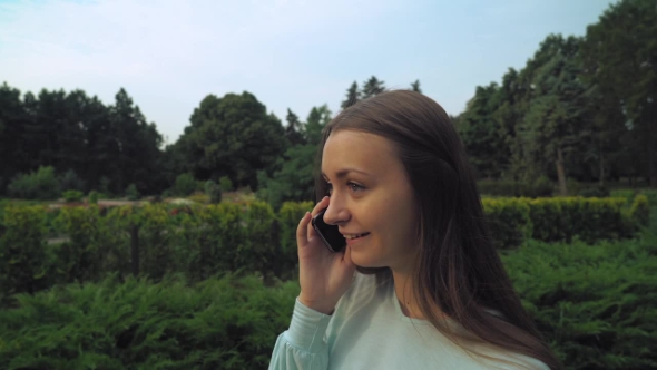 Young Brunette Girl Slowly Passes Through The Park And Talking On The Phone. alt