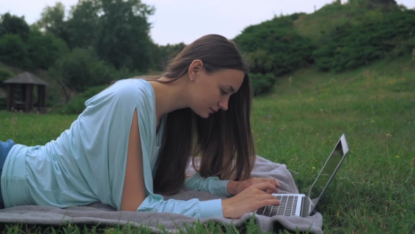 A Young Woman Lies On Lawn And Gaining a Message On The Computer. Laughing, Rejoicing. alt
