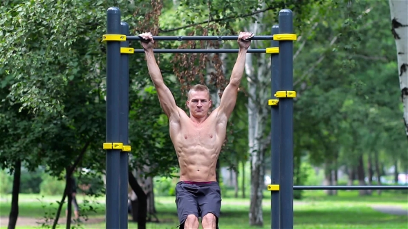 Athletic Man Doing Lifting Legs On Horizontal Bar In City Park. Athletic Man Exercise The Abdominals