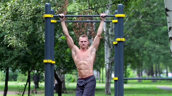 Athletic Man Doing Lifting Legs On Horizontal Bar In City Park. Athletic Man Exercise The Abdominals