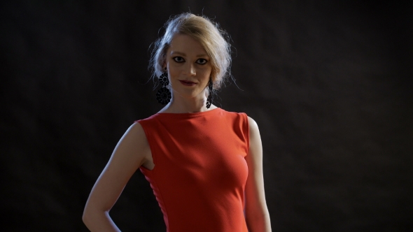 Chic Woman In Red Dress Standing On Black Background And Laying Hand On Hip, Then Crosses Her Arms