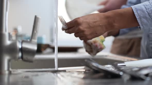 Close Up Footage of Dark Skinned Female's Hands Washing Fork Under Water Jet Using Dishwashing alt