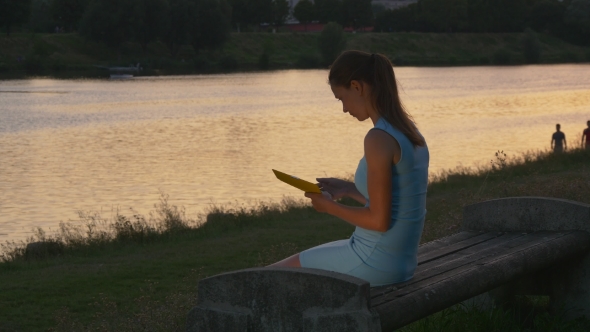 Woman Reads Electronic Book At Sunset On The Bench