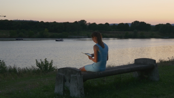 Young Woman Reads An E-book At Sunset In The Park