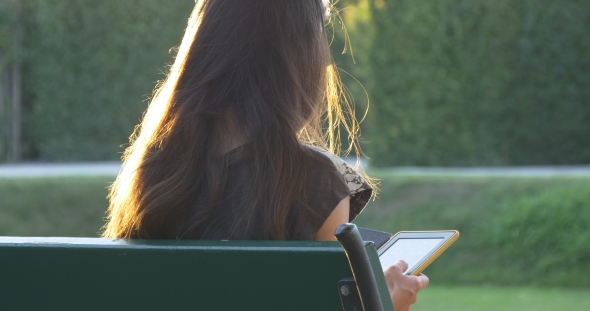 Female With Sunlight On Her Hair Reads E-book In The Park