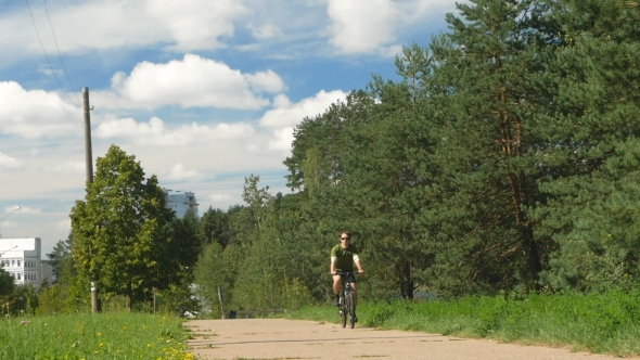 Male Cyclist Riding On The Track. Beautiful Clouds And Dense Trees Nearby. 