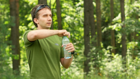 Young Male Cyclist Drinks Water From a Bottle In The Park. Green T-shirt And Sunglasses