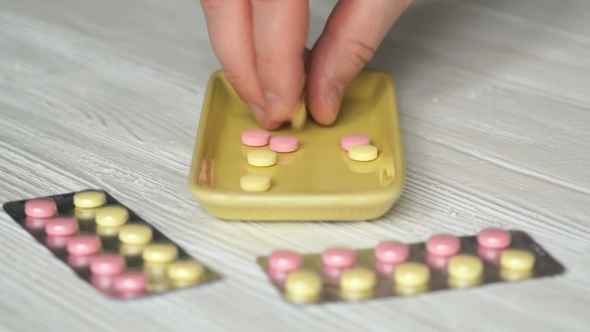 Hand Calculates Pills In a Yellow Container