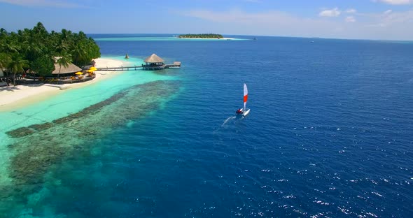 Aerial drone view of a man and woman sailing on a boat to a tropical island. alt