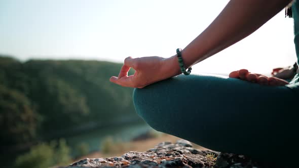 Healthy Woman Sitting in Lotus Pose and Meditating on High Cliff Above River alt