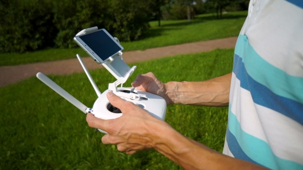 a young man in a t-shirt uses a remote controller to control the quadcopter alt