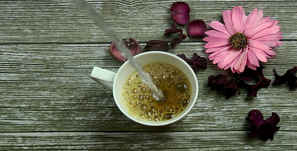 Pouring Hot Water into Cup of Coffee with Flowers on Wooden Background