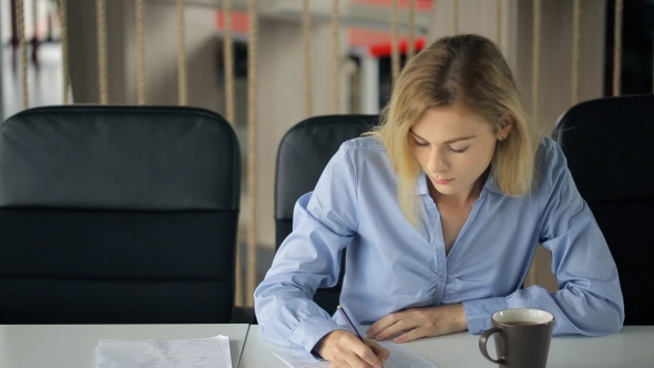 Young Attractive Blond Woman Sitting At a Table And Fills In Questionnaire With a Pencil. alt