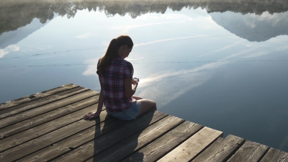 Woman Texts In Smartphone Sitting At The Lake