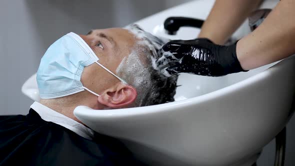 Female hairdresser hands in rubber gloves washes the head of a medical mask man. A hairdresser with