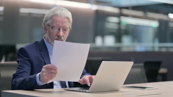 Old Businessman Reading Documents Working on Laptop alt