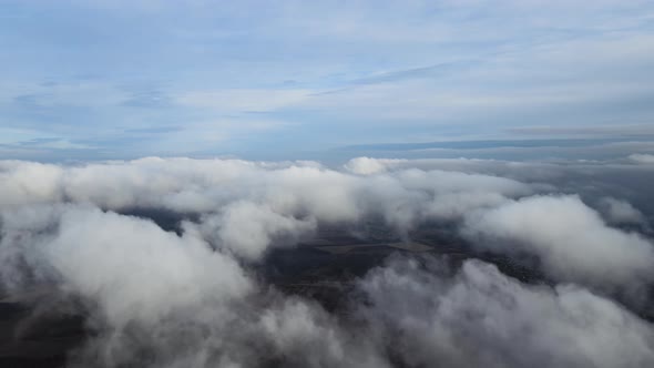 Aerial View From High Altitude of Distant City Covered with Puffy Cumulus Clouds Flying By Before alt