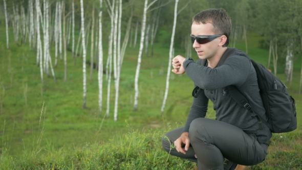 Young Man In Sunglasses Speak In Smart Watch. Against The Background Of Beautiful Nature: Green
