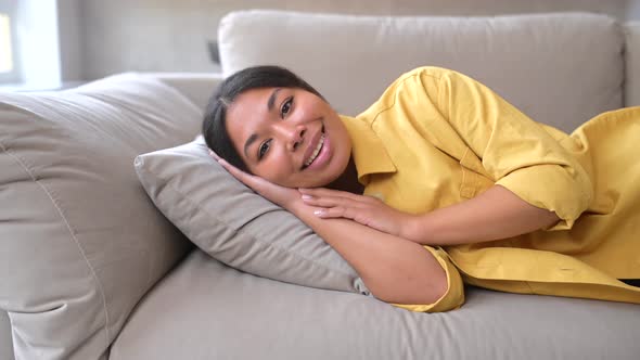 Serene Relaxed Young AfricanAmerican Woman Looking at Camera Lying Down on the Sofa