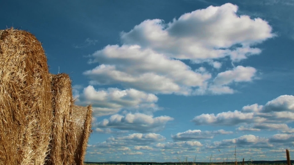 Stubble Field With Straw Bales Under Cloudy Sky.