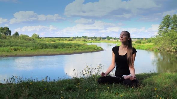 Sport Girl In Lotus Position Sitting On The River Bank