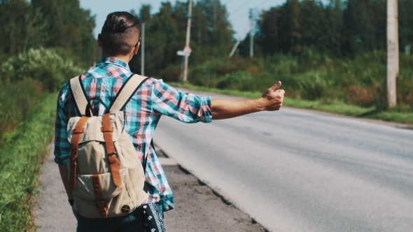 Back Side of Young Boy With Backpack Hitchhiking at Road in Summer Sunny Day. alt