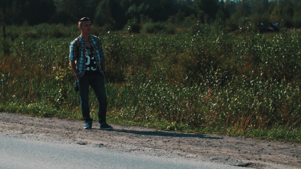 Young Boy With Backpack Hitchhiking At Road. Traveler. Thumb Up. Roadside. alt