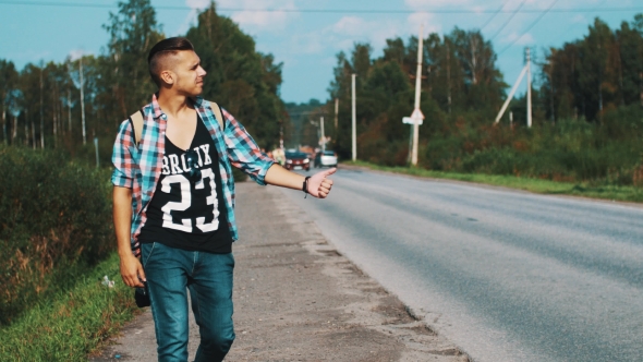 Boy With Backpack Walking Along Roadside. Hitchhiking. Holding Thumb Up. alt