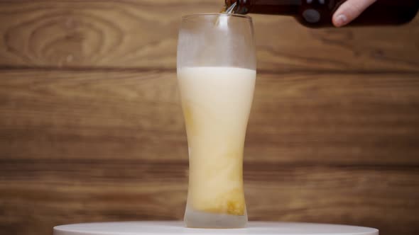 Beer with foam is poured into a frozen glass. Wooden background.