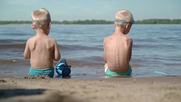 Two brothers sit at the water's edge and play their childish games. alt