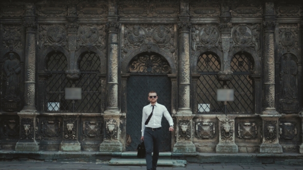 Serious Businessman With a Briefcase In Front Of An Office Building Fixing His Tie alt
