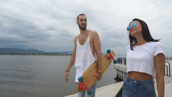 Guy And a Girl With Long Boards Walk Along The Waterfront And Talk