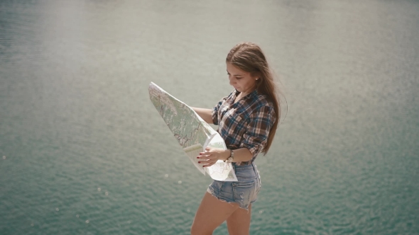 Young Active Backpacker Girl Checking With Map Near Water Surface Of Mountain Lake At Sunny Day