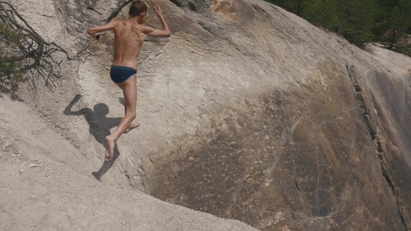 Man Leaping On The Rocks Near Lakeshore And Jumping Off Cliff Into The Water. Summer Fun Lifestyle