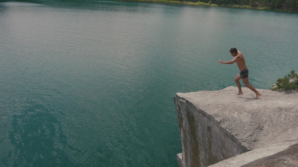 Man Jumping Off Rock Slope Into The Water. Summer Fun Lifestyle