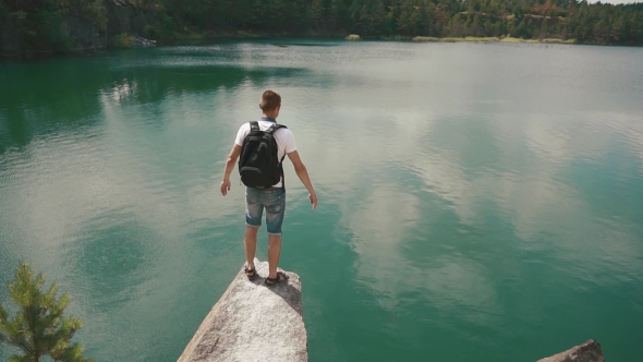 Young Active Man Widens His Hands On Rock Slope Upon Calm Mountain Lake Surface