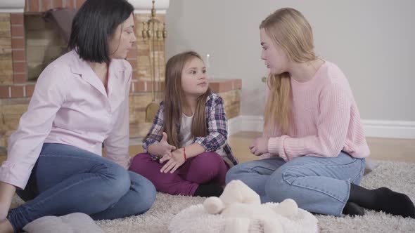 Portrait of Happy Caucasian Family Sitting on Soft Carpet in Front of Fireplace and Talking. Mother alt
