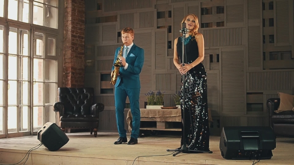 Jazz Vocalist in Glowing Dress and Saxophonist in Blue Suit Perform on Stage. alt