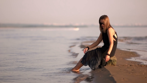 Girl In a Black Dress Sitting On a Rock By The River Feet In The Water
