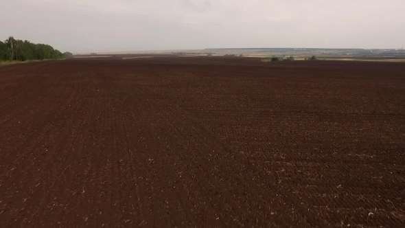 Drone Flying Up Over Black Plowed Field, Rising High And Showing Beautiful Countryside Landscape
