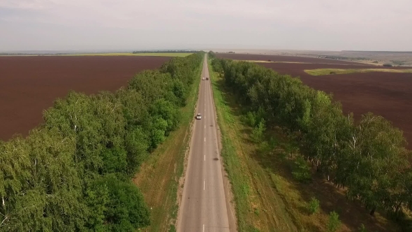 Drone Flying Over Asphalt Road Between Two Plowed Fields In Countryside, Cars Moving Down