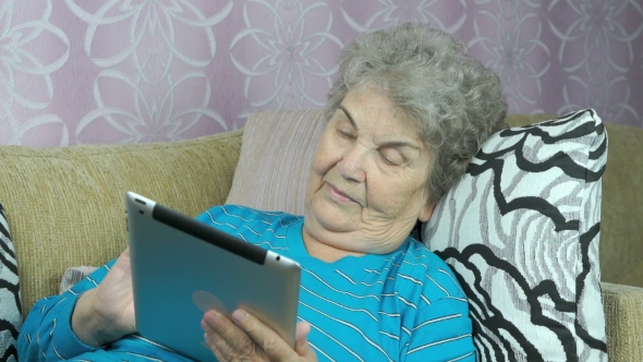 Elderly Woman Holds a Digital Tablet Indoors
