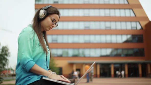 Girl Listening To Music On Headphones And Typing On a Laptop Keyboard.