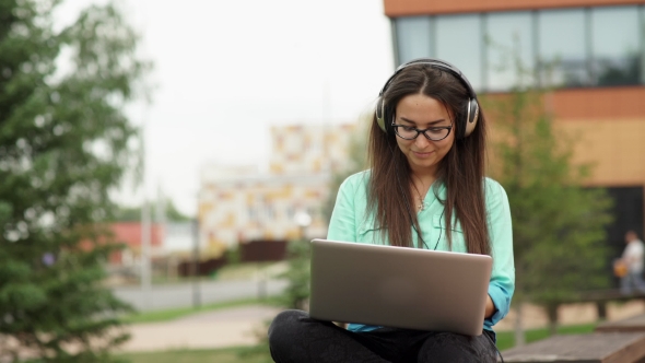 Girl Listening To Music On Headphones And Typing On a Laptop Keyboard